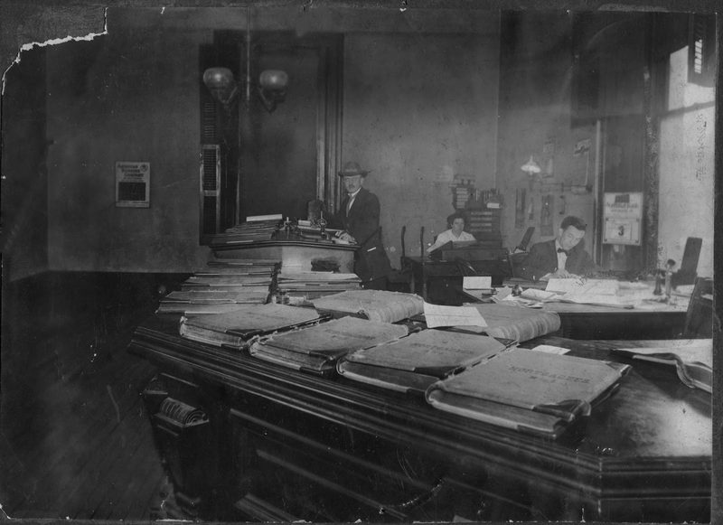 Interior view of Recorder's Office in Courthouse. Recorder at time was Wm. H. Trude, standing at counter; clerks were Blanche Beck and Oscar Vaughn. Photo given by Mrs. Oscar Vaughn. — Recorders Office Courthouse.jpgcropfix