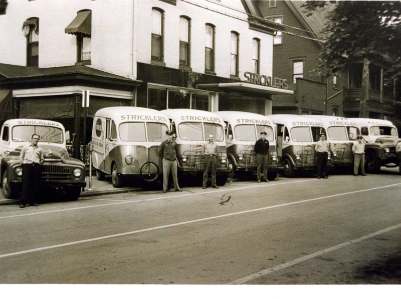 Six delivery truck drivers for Strickler's Dairy pose with their trucks in front of STrickler's Dairy Store at 8th & Washington Sts. They are identified as: Gob Allison, Carl Ergler, Dusty Cramer, Gerald Turbott, Charles Querry, and Bill Scalia. — Stricklers Route Trucks
